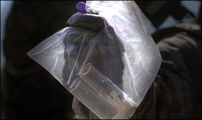 a gloved hand holding a plastic bag containg two sample vials